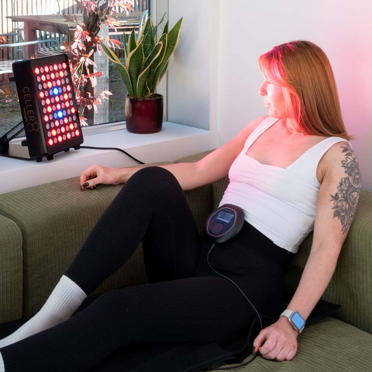 Person using a red light therapy device on a couch while using travel mat