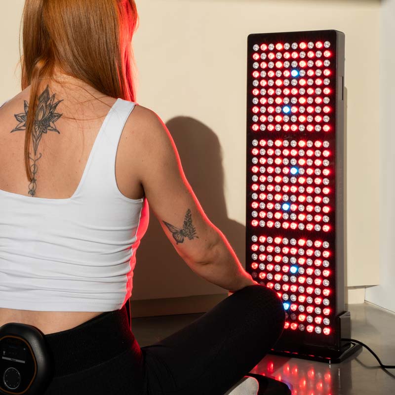 Women sat on CELLER8 PEMF full body mat with CELLER8 wrapped around waist sitting in front of CELLER8 half body red light panel 