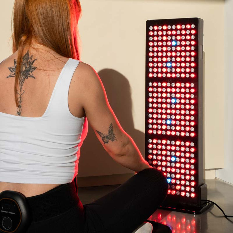 Women sat on CELLER8 PEMF full body mat with CELLER8 wrapped around waist sitting in front of CELLER8 half body red light panel 