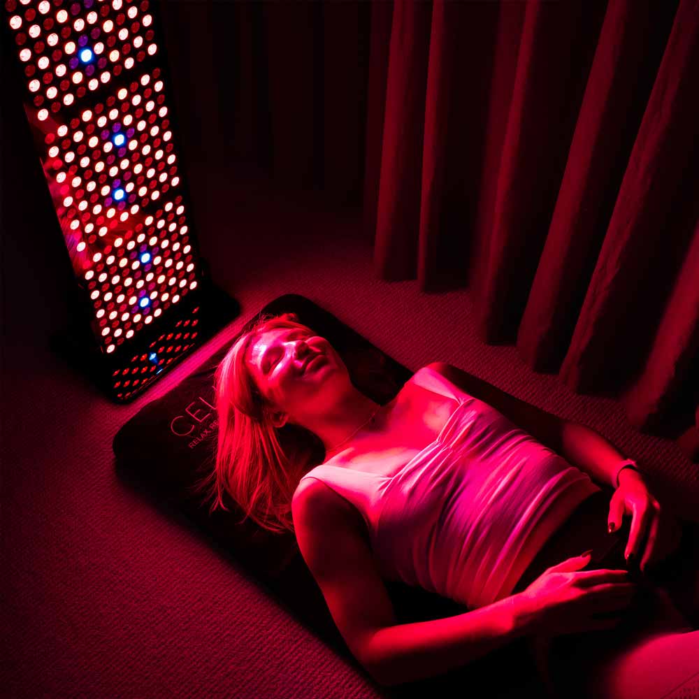 Lady laying on CELLER8 full body mat while using CELLER8 half body red light panel