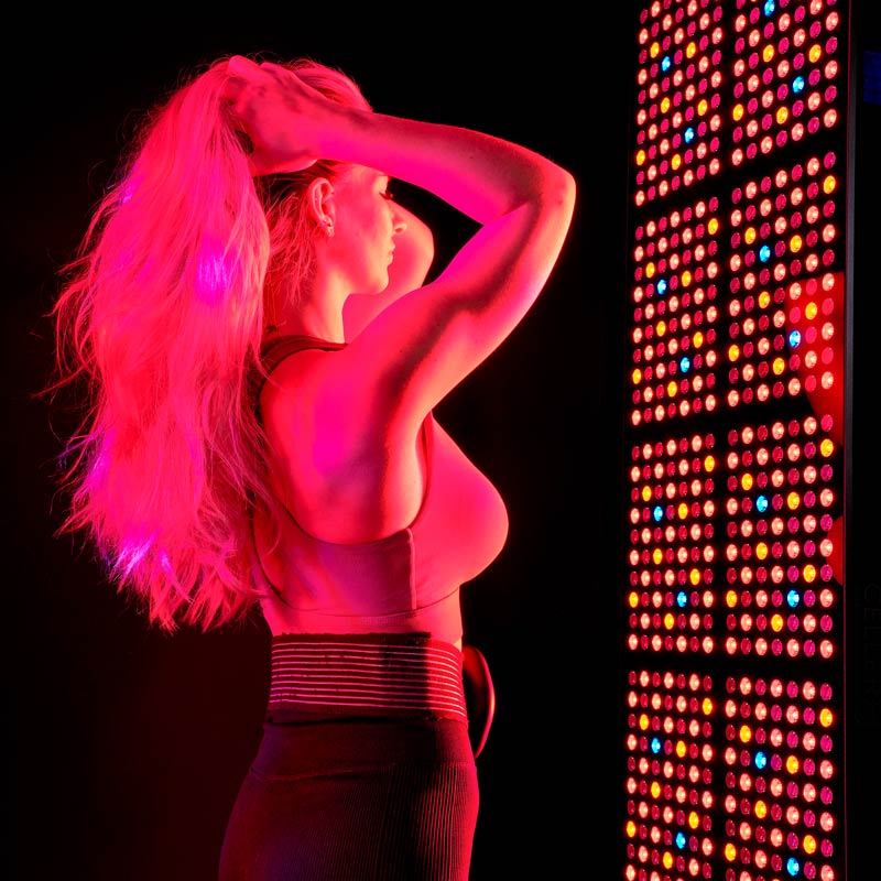 Lady stood in front of CELLER8 full body red light panel with CELLER8 PEMF around waist