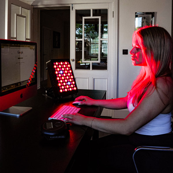 Person using a computer with red light therapy device