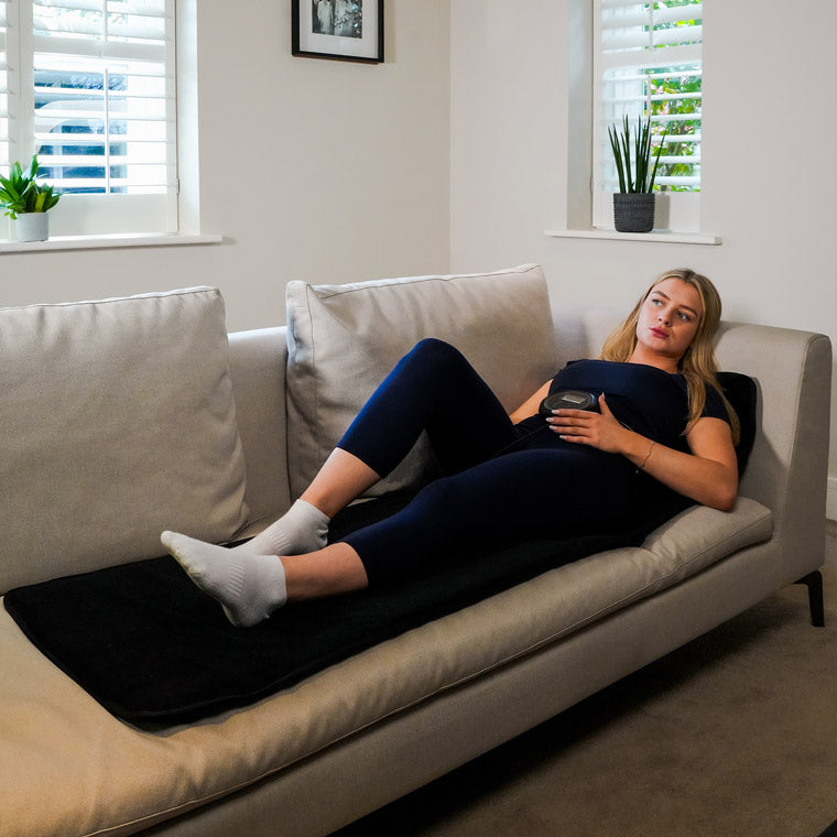 Women laying on full body mat on sofa with CELLER8 around waist