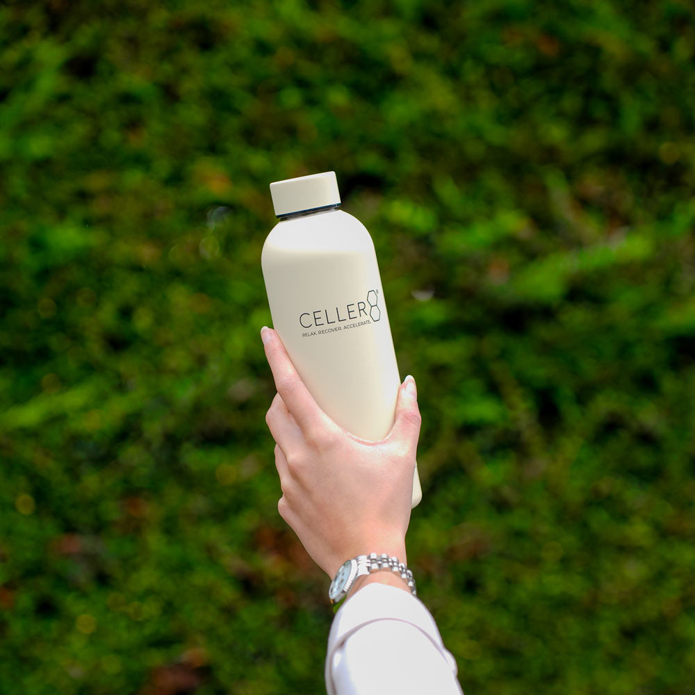Tan CELLER8 water bottle in front of trees 