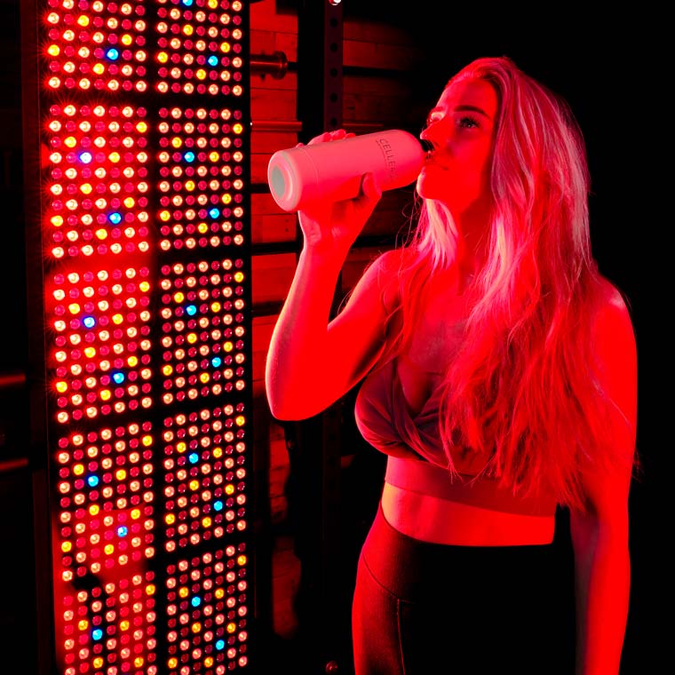 Women drinking water in front of red light panel
